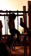 A child playing tightrope walker on a balance course of an amusement park. Backlit sun circle with...