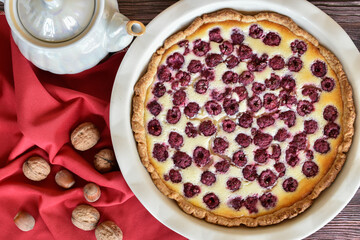 Homemade sour cream raspberry pie, baking dish, red napkin over wooden table, pearlescent teapot....