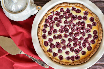 Homemade sour cream raspberry pie, baking dish, red napkin over wooden table, pearlescent teapot, metal cake shovel. Sweet pastry dessert, tasty food, vintage background.