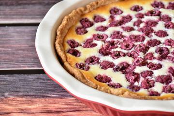 Homemade sour cream raspberry pie on wooden table, red and white baking dish. Sweet pastry dessert, tasty food, vintage background.