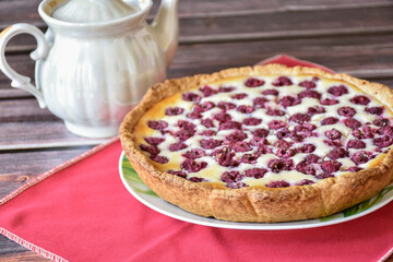 Homemade sour cream raspberry pie on wooden table, red napkin, pearlescent teapot. Sweet pastry dessert, tasty food, vintage background.