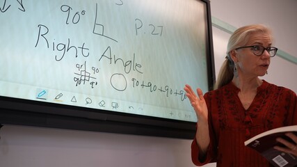 Closeup of happy female teacher writing on an interactive whiteboard teaching geometry math in a school classroom.