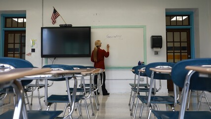 Wide angle view of woman teacher using an interactive whiteboard blackboard in an empty classroom teaching geometry math.