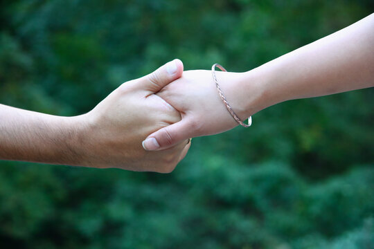 A close up of a man's and a woman's hands holding each other. The woman is wearing a bracelet. Background is deep green.