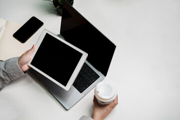 Holding coffee and black screen touch pad screen for mockup multimedia technology device with tablet computer and plant on table indoor workspace working on reviewing and reading application document