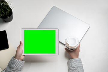 Holding coffee and green screen touch pad screen for mockup multimedia technology device with tablet computer and plant on table indoor workspace working on reviewing and reading application document
