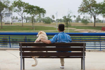 Handsome young man and his Labrador retriever dog sitting on a wooden bench in the park. The man...