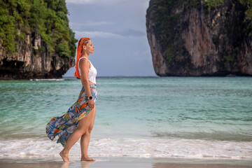 A beautiful girl stands on a sunny sandy beach. The famous Maya Bai. Sunny morning. Beautiful sea.