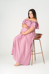 Plus size pregnant woman in dress on gray background, maternity clothes, pregnancy concept