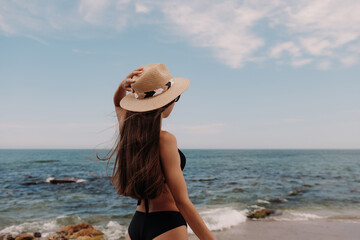 Fototapeta na wymiar Rear view of beautiful woman in swimwear adjusting hat while enjoying sea view on the beach