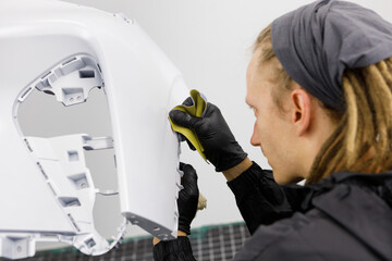 A man prepares a car body element for painting after an accident with the help of abrasive paper in a car repair shop. Recovery bumper after a collision