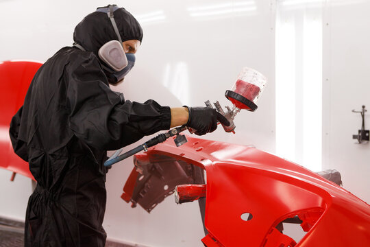Applying paint to the bumper. Paint the bumper with varnish using an airbrush. Close-up of a spray gun being used by a mechanic while painting a car bumper in a spray booth