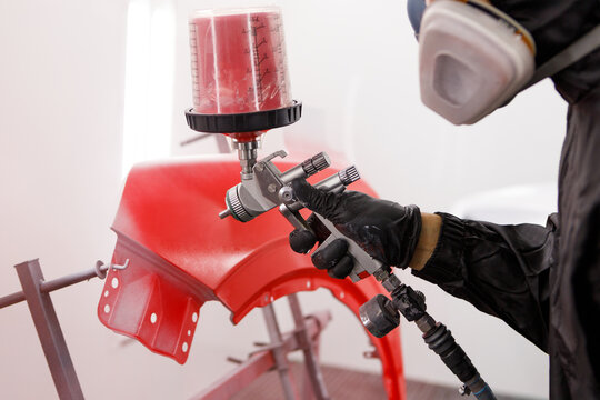 Car renovation and detailing process. Close-up perspective of car part being varnishing in paint spray booth by a hand in a protective glove holding spray gun