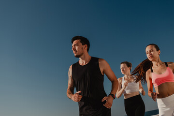 Three confident young people in sportswear looking concentrated while jogging outdoors together