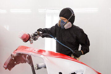auto repair under warranty. car painter paints the hood of the car in the spray booth in red