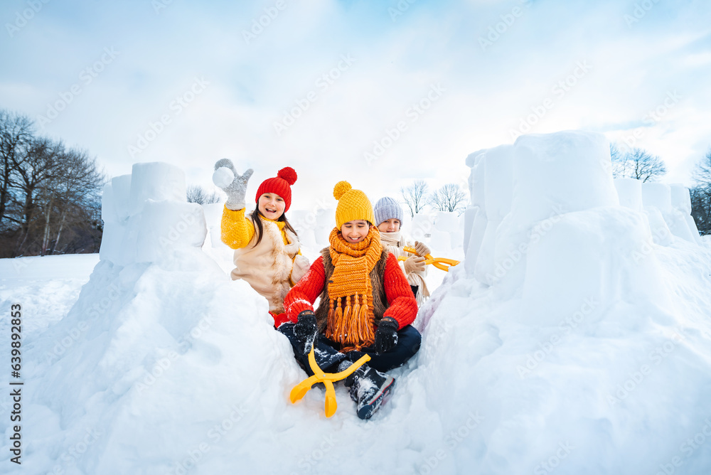 Wall mural Group of children make snowballs for snowball fights. Children play in snow fort made of ice blocks. Active winter outdoor games.