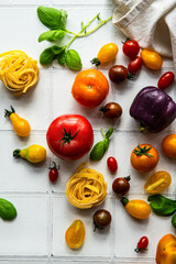 Ingredients for vegetable pasta.
Dry tagliatelle nests, variety of fresh tomatoes, peppers, basil and mozzarella ball on white tile background.