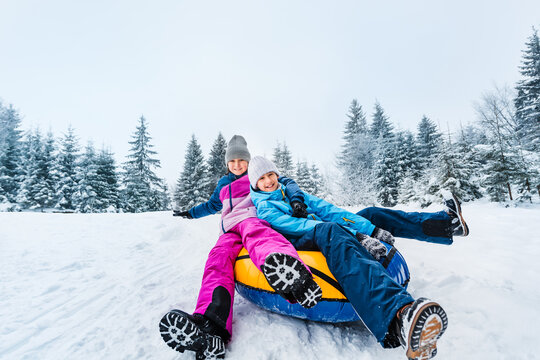 Smiling children ride down on inflatable tubing sleds. Inflatable sleds for active winter family recreation. Wide angle shooting.