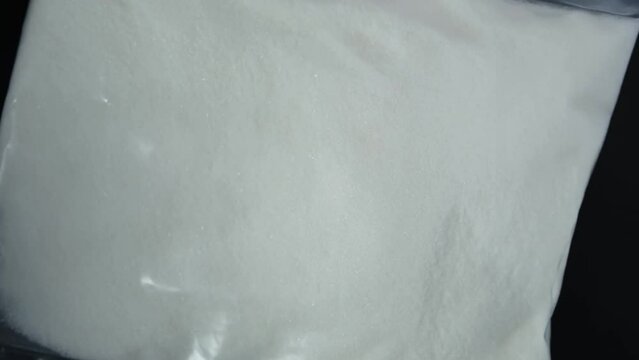 Sodium dihydrogen citrate powder in plastic bag, close-up. Food additive E331, preservative and flavoring. 4K video, Rotating. Sodium citrate used in food industry as color fixative product.