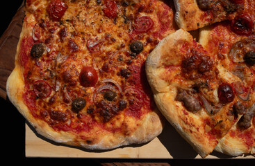 Large homemade pizza with tomatoes, oregano, onions, salsiccia and cheese. The pizza is partially cut into pieces and lies on a wooden board
