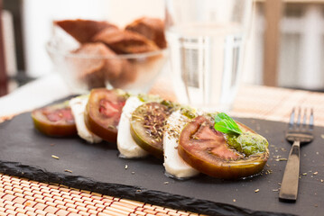 caprese salad with mozzarella, black tomatoes and pesto on black stone plate