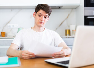 Obraz na płótnie Canvas Upset man with laptop and utility bills in kitchen