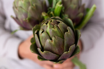 Obraz premium close-up shot. hands hold artichokes on a light background. the concept of healthy eating and plant farm organic food