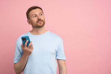 Pensive man dreamer holding mobile phone think about future prospects isolated on pink background. Thoughtful male with smartphone considering mortgage proposal, pondering job offer studio copy space 