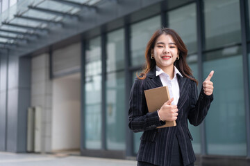 Beautiful Woman Going To Work With book Walking Near Office Building. Portrait Of Successful Business Woman Holding a book