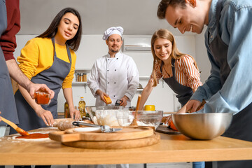 Group of young people with Italian chef preparing pizza during cooking class in kitchen