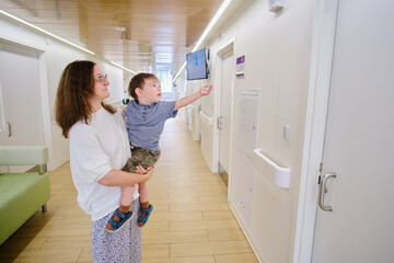 The child and his mother in the clinic corridor, looking at the door of the treatment cabinet where they will soon see the doctor. Kid boy aged two years (two-year-old)