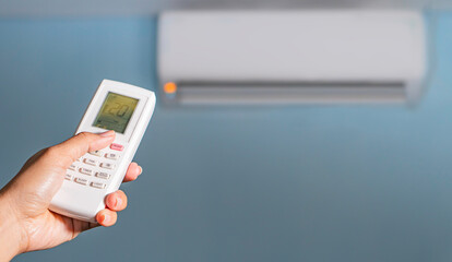 Air conditioner temperature adjustment with remote controller in room at home.