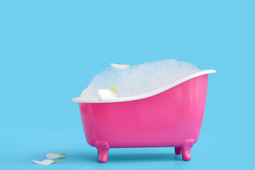 Naklejka premium Small bathtub with soap foam and flower petals on color background