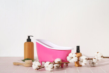 Fototapeta na wymiar Composition with small bathtub, bath supplies and cotton branch on color tile table