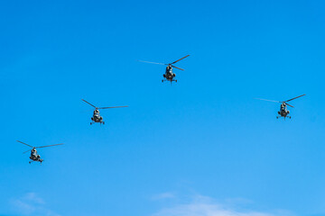 Four helicopters fly in formation across a clear blue sky