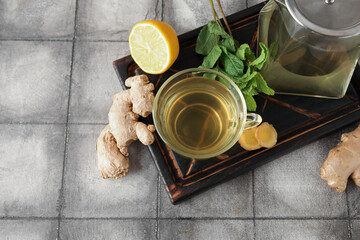 Glass cup of ginger tea with lemon and mint on grey tile table