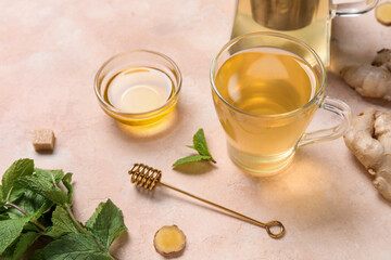 Glass cup of ginger tea and bowl with honey on pink background