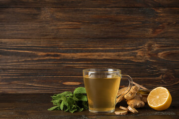 Glass cup of ginger tea with lemon and mint on wooden background