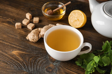 Cup of ginger tea and bowl with honey on wooden background