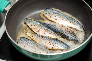 Raw fish fillet sprinkled with salt and spices is fried in a frying pan. Cooking fish.