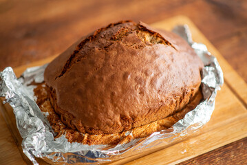 Loaf of freshly made bread or cupcake in foil on a wooden background.