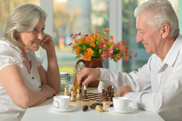 Older woman playing chess with her smart elderly husband at home
