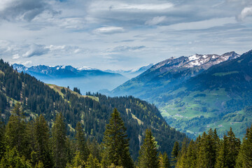 Spring sunlight illuminating the forests, farms and the partially snow-covered mountains of the...