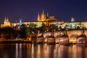 Fototapeta na wymiar Night time view of Charles Bridge across the Vltava River in the heart of Prague with St. Nicholas Church to the left and Prague Castle and St. Vitus Cathedral lit up on the hilltop in the background