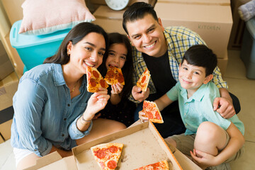 Smiling family with children enjoying eating pizza after unpacking at theirr new house