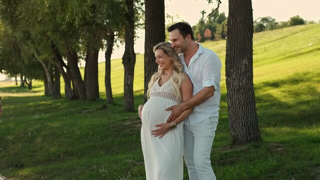 Children and father hug and kiss the belly of a pregnant mother.