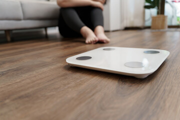 Fototapeta premium Sad woman with fat upset bored of dieting Weight loss fail&nbsp; Fat diet and scale sad asian woman on weight scale at home weight control