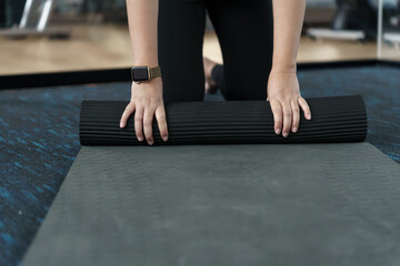 Fitness woman folding exercise mat before working out in yoga studio. rolling Yoga mat  after training healthy lifestyle