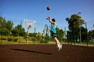 Active teenager boy playing basketball on street outdoor court