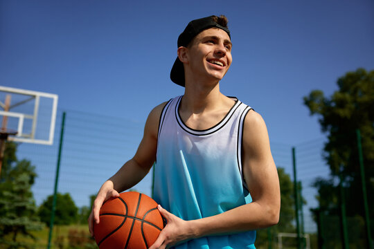 Happy smiling teenager basketball player with ball practicing on outdoor court